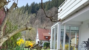 Une maison moderne avec un jardin, un bâtiment aux toits rouges en arrière-plan et un ciel dégagé.