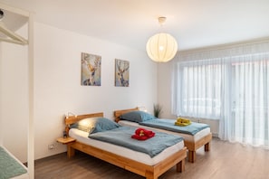 A bedroom with two wooden beds, a large window with sheer curtains, and artwork on the wall.
