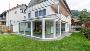 Une maison moderne dotée d’une extension en verre, d’une pelouse bien entretenue et offrant une vue sur les environs.