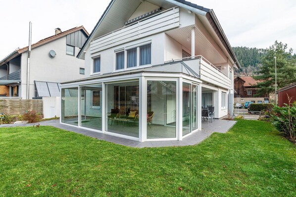 Une maison moderne dotée d’une extension en verre, d’une pelouse bien entretenue et offrant une vue sur les environs.