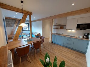 A modern kitchen with wooden cabinets, a dining area with a table and chairs, and a stone wall in the background.