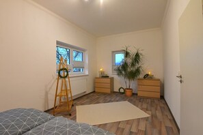 A small, well-lit room with a bed, a wooden ladder, a radiator, a small table with a plant, a potted plant, and a window. - Apartment 'Ferienwohnung Sonneberg' with Private Terrace and Wi-Fi (Sonneberg)