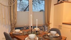 A dining table set with white plates, bowls, and glasses, a white candle, and a vase with dried flowers.