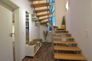 A modern interior with a wooden staircase, a white bench with fur, and potted plants. - Apartment 'Ferienwohnung Sonneberg' with Private Terrace and Wi-Fi (Sonneberg)