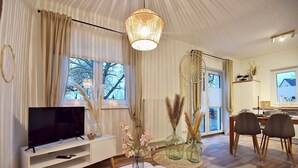 A modern living room with a TV, white furniture, a round table, and decorative plants.