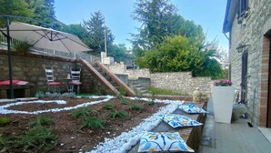 A garden with a stone wall, a wooden staircase, and outdoor seating with umbrellas.