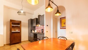 A dining area with a wooden table and chairs, a kitchen in the background, and pendant lighting.