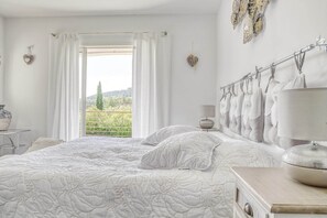 Quarto com uma cama grande, uma mesa de cabeceira com abajur e vista para o verde lá fora.