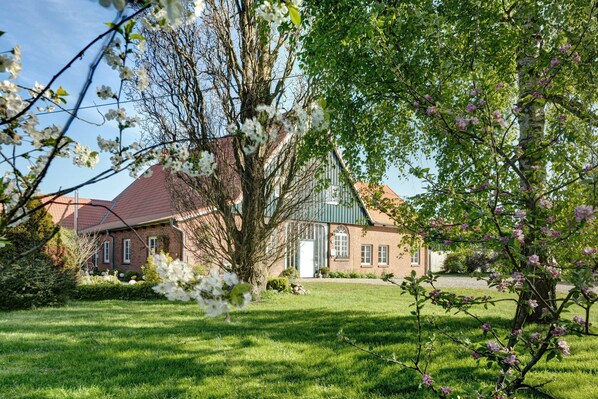 A brick building with a green roof, surrounded by a well-maintained lawn and flowering trees.