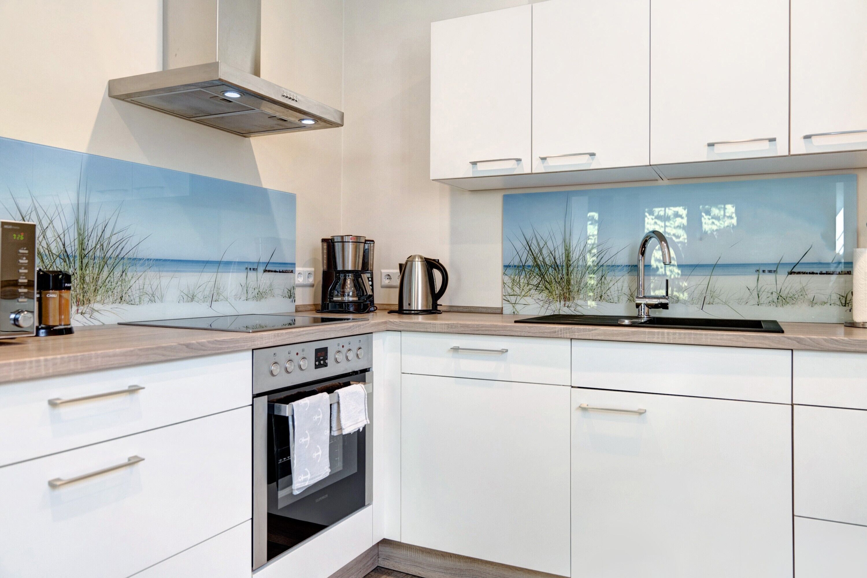Eine moderne Küche mit weißen Schränken, einem Edelstahlbackofen, einer Kaffeemaschine und Meerblick durch ein Fenster.