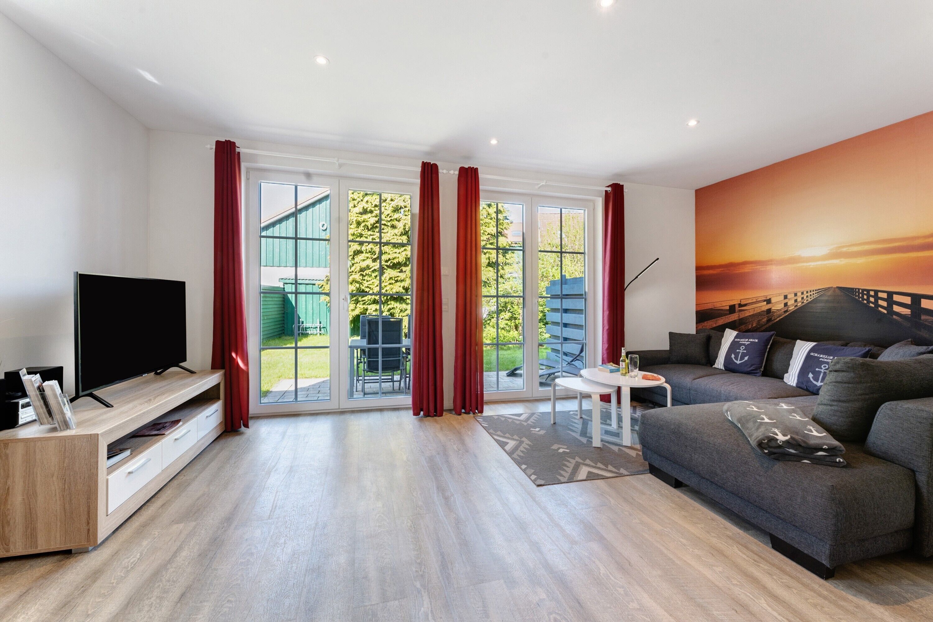 Un salon moderne avec un téléviseur à écran plat, un canapé gris et une grande fenêtre ornée de rideaux rouges.