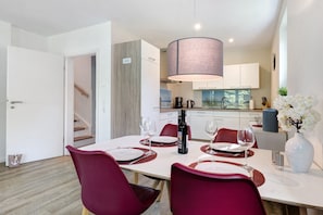 A modern dining area with a table set for four, a wine bottle, and a vase with flowers.