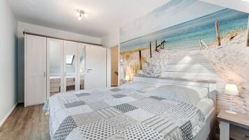 Ein Schlafzimmer mit einem großen Bett, einem Bild mit Strandmotiv, einem Kleiderschrank und einem Schreibtisch mit Lampe.