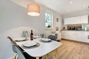 Un coin repas avec une table dressée pour deux personnes, un luminaire suspendu et une vue sur la cuisine.
