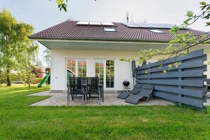 Une maison avec un patio, un barbecue et un toboggan à l’arrière-plan.