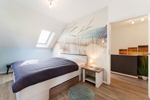 Une chambre à coucher avec un lit, une table de chevet, une lampe et une vue sur le ciel grâce à une lucarne.
