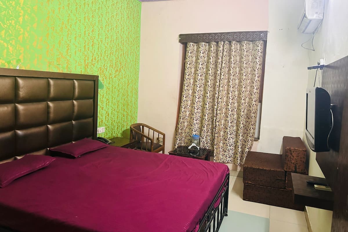 A bedroom with a bed, a wooden nightstand, a TV, and a window with curtains.