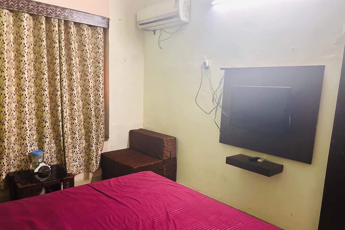 A hotel room with a bed, a small table with a water bottle, a chair, and a mounted TV.