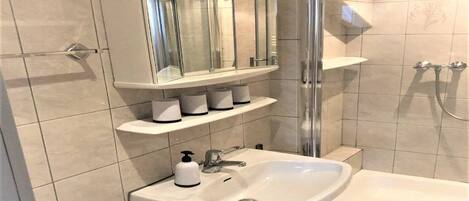 Ein modernes Badezimmer mit einer Duschkabine, einem weißen Waschbecken und einem Waschtisch mit Spiegel und Ablageflächen.