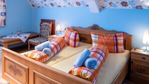 A double bed with plaid bedding, a nightstand with a lamp, a wooden dresser with floral carvings, and a floral-patterned ceiling. - Ferienwohnung in Lauterbach im Schwarzwald (Lauterbach)