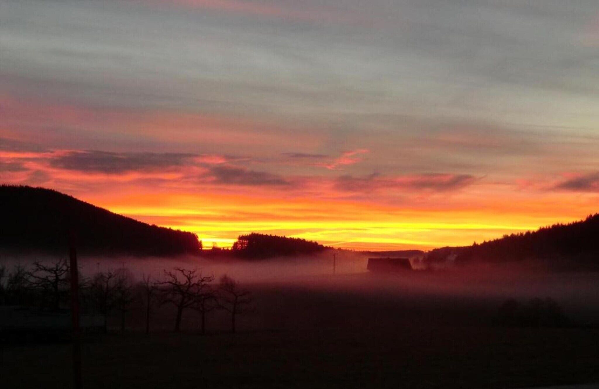 A sunset over a hilly landscape with a misty foreground.
