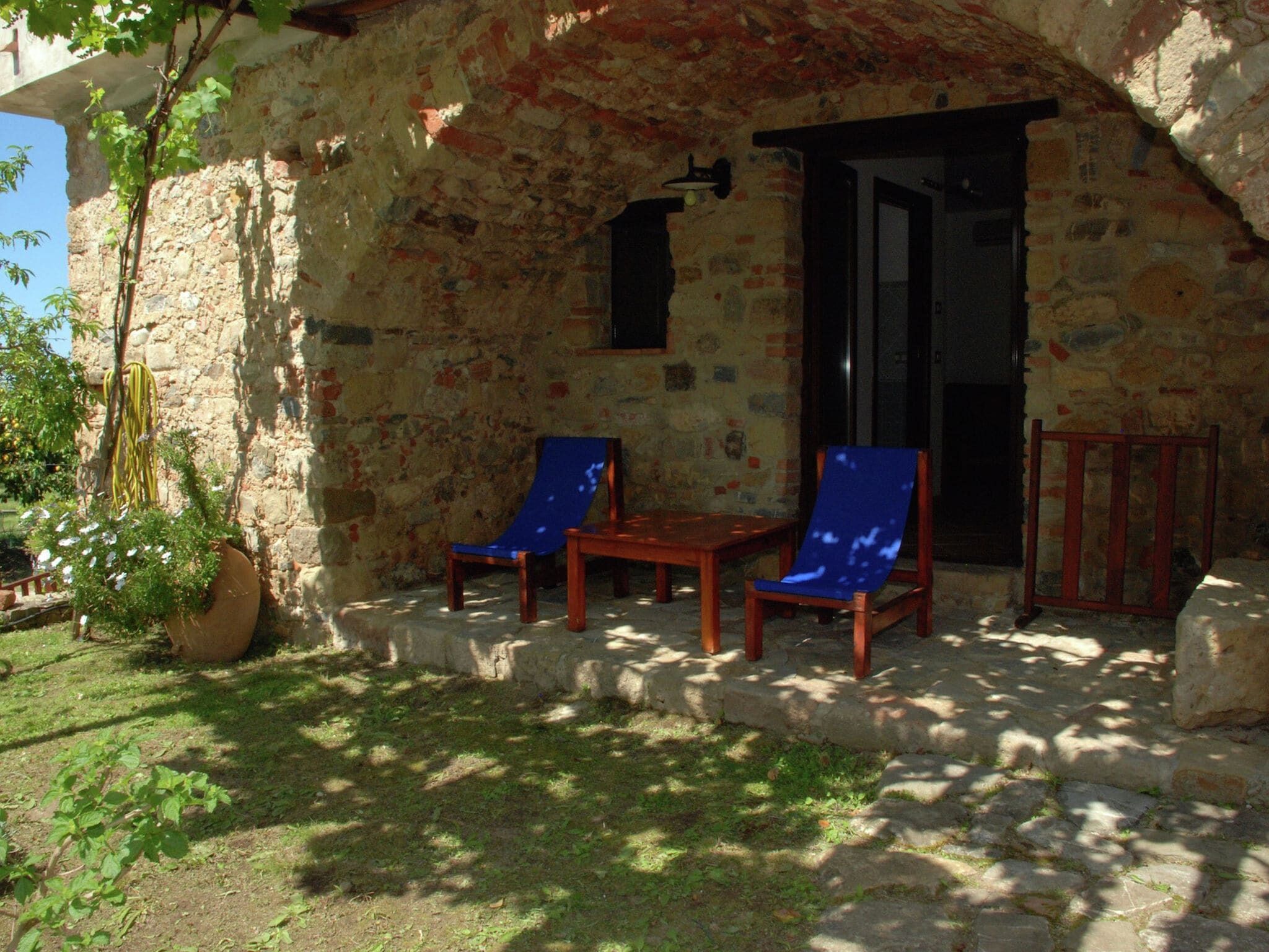 A stone building with two wooden chairs and a table outside.