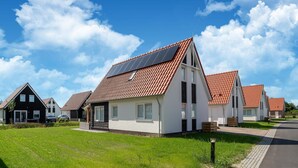 A row of modern houses with red-tiled roofs and solar panels, set in a green landscape with a paved road. - Coastal Getaway w/ Sauna (Scherpenisse)