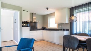 A modern kitchen with white cabinets, a black countertop, and a dining area with a table and chairs. - Coastal Getaway w/ Sauna (Scherpenisse)