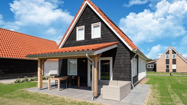 A modern house with a black exterior, red roof, and a covered patio with outdoor furniture. - Coastal Getaway w/ Sauna (Scherpenisse)