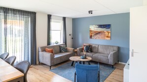 A modern living room with two sofas, a coffee table, and a dining area with chairs. - Coastal Getaway w/ Sauna (Scherpenisse)
