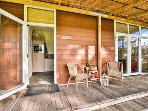 A wooden deck with wicker chairs and a small table, a kitchen area with a microwave, and a sign reading "Hotel & Chalet". - Holiday Home in Tripscompagnie near Nature (Tripscompagnie)
