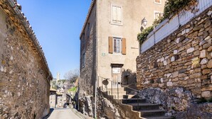 A narrow street flanked by stone buildings with a staircase leading to a door.