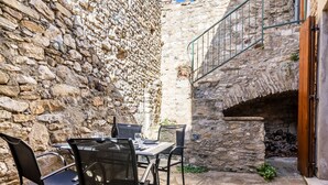 A stone-walled outdoor dining area with a table and chairs, a stone floor, and a small fire pit.