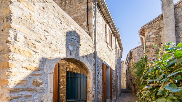 A narrow cobblestone street flanked by stone buildings with arched doorways and wooden shutters.
