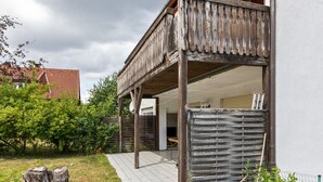 A wooden balcony attached to a building with a tiled roof, surrounded by greenery and a paved walkway. - Nature Escape in Fuldabruck (Fuldabrück)