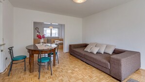 A room with a wooden herringbone floor, a brown sofa with cushions, a dining table with chairs, and a vase with flowers. - Nature Escape in Fuldabruck (Fuldabrück)