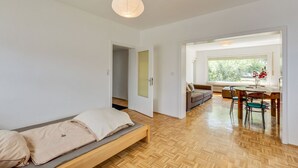 A modern room with a wooden floor, a bed with beige bedding, a dining table with chairs, and a window with a view of greenery. - Nature Escape in Fuldabruck (Fuldabrück)