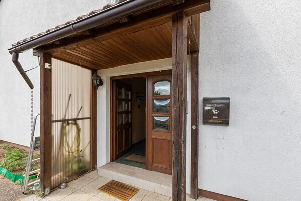 A wooden entrance with a metal door, a small step leading inside, and a mailbox on the wall.