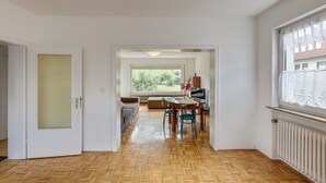 A spacious room with a wooden herringbone floor, a dining area with a table and chairs, a sofa, and a large window with a view of greenery. - Nature Escape in Fuldabruck (Fuldabrück)