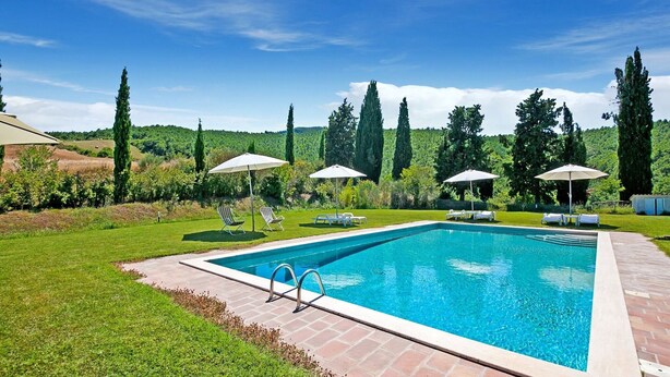 A rectangular swimming pool with a tiled deck, surrounded by grass and trees.