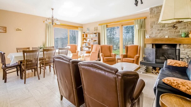 A cozy living room with a fireplace, a dining area with a table and chairs, and a bookshelf.