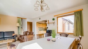 A dining area with a table set for four, surrounded by wooden chairs, a sofa, and a lamp.