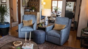 A living room with two armchairs, a coffee table, and a lamp. There is a bookshelf and a dining area in the background. - Cozy family home minutes from The University of Puget Sound! (Tacoma)