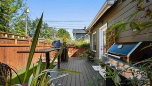 A wooden deck with a barbecue grill, a wooden table, and a house with a window. - Cozy family home minutes from The University of Puget Sound! (Tacoma)