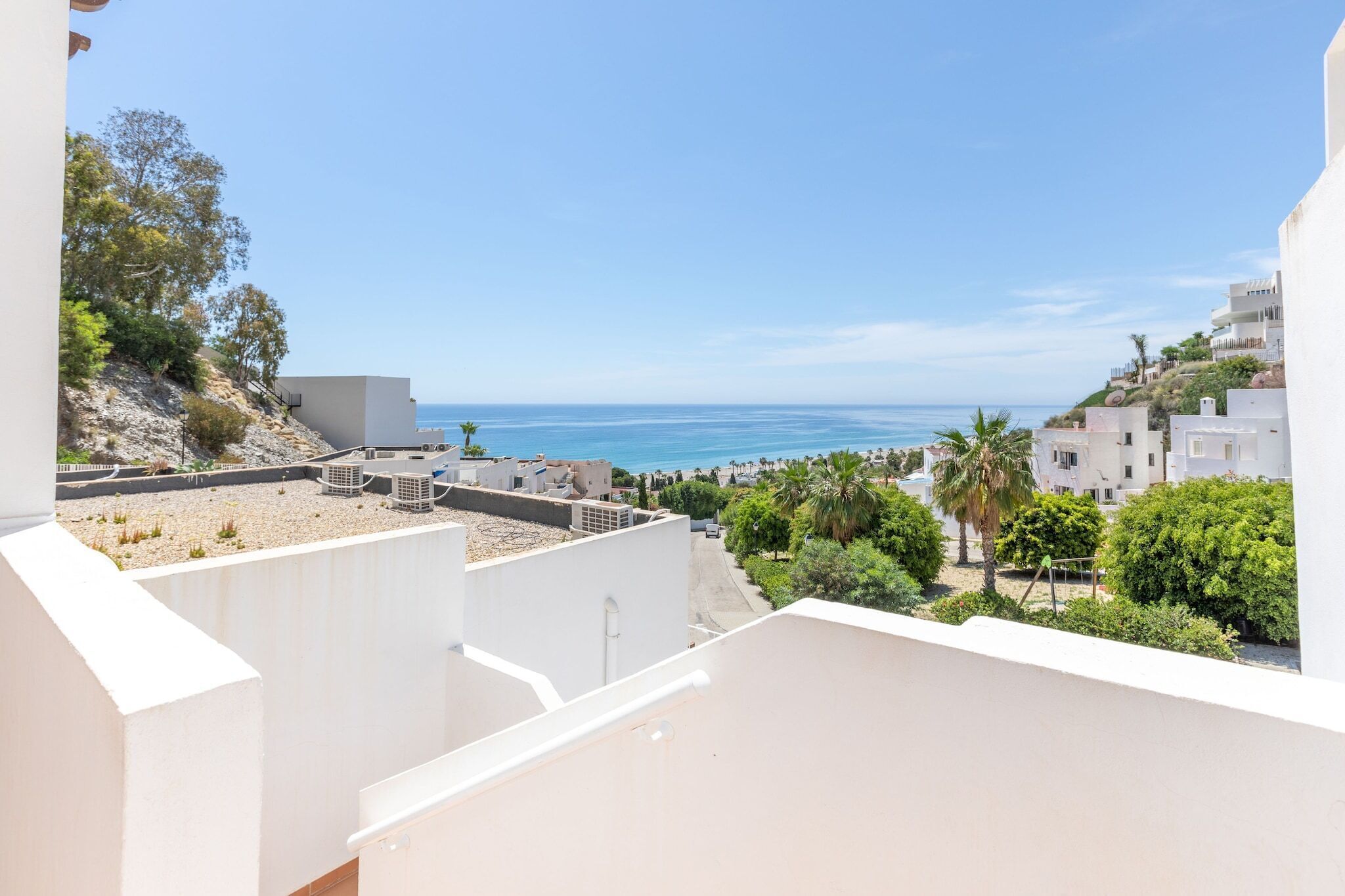 A coastal residential area with white buildings, a clear blue sky, and a view of the sea.