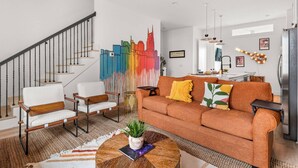 Uma sala de estar moderna com escada, um mural colorido, um sofá com almofadas e uma área de cozinha com geladeira.