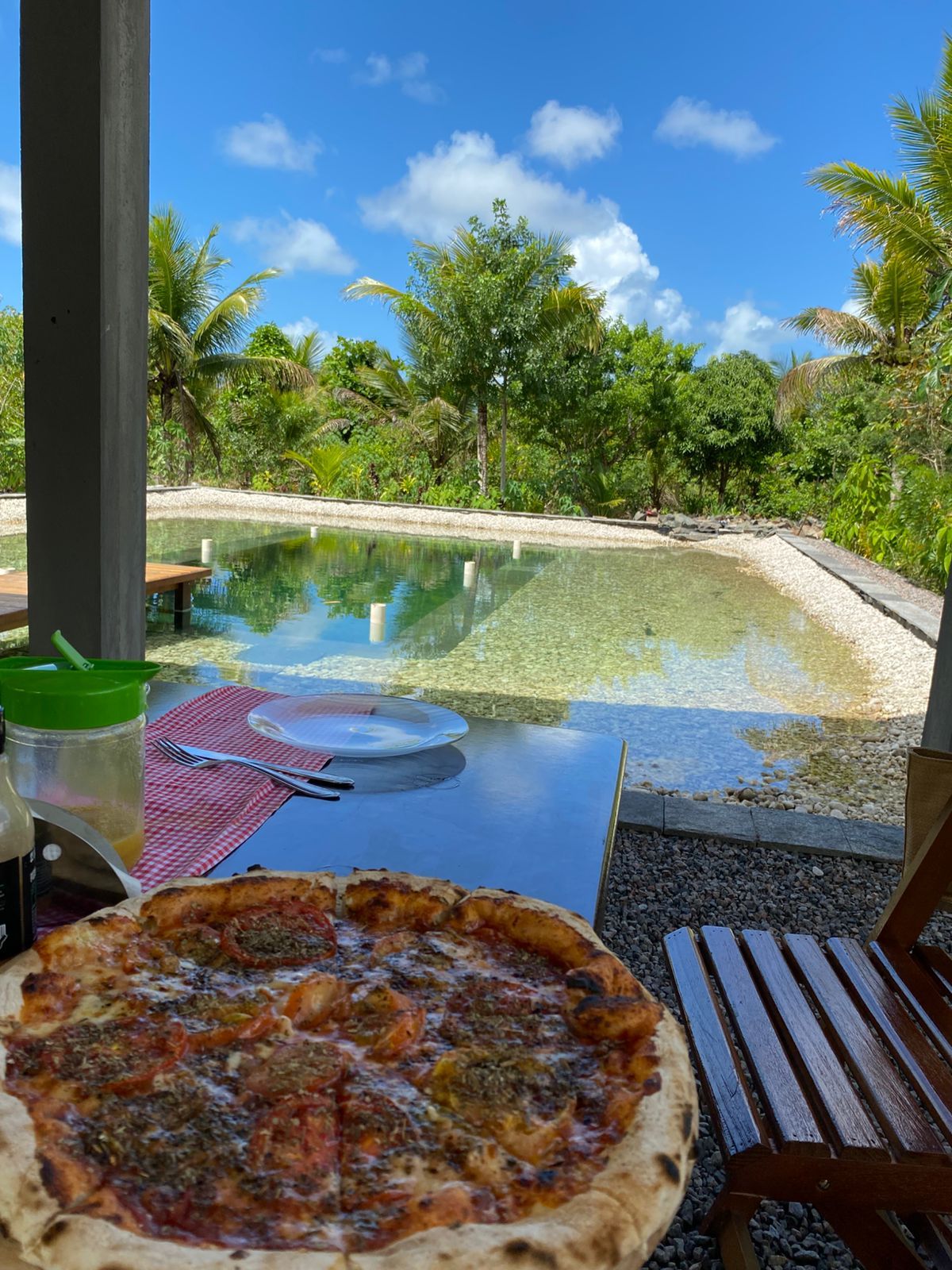 Een eettafel met een pizza, een groene verpakking en een rood-wit geruit servet.