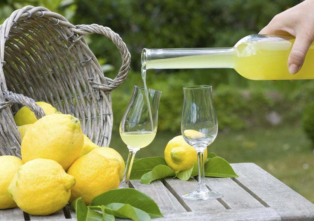 A wicker basket filled with lemons and two glasses on a wooden table.