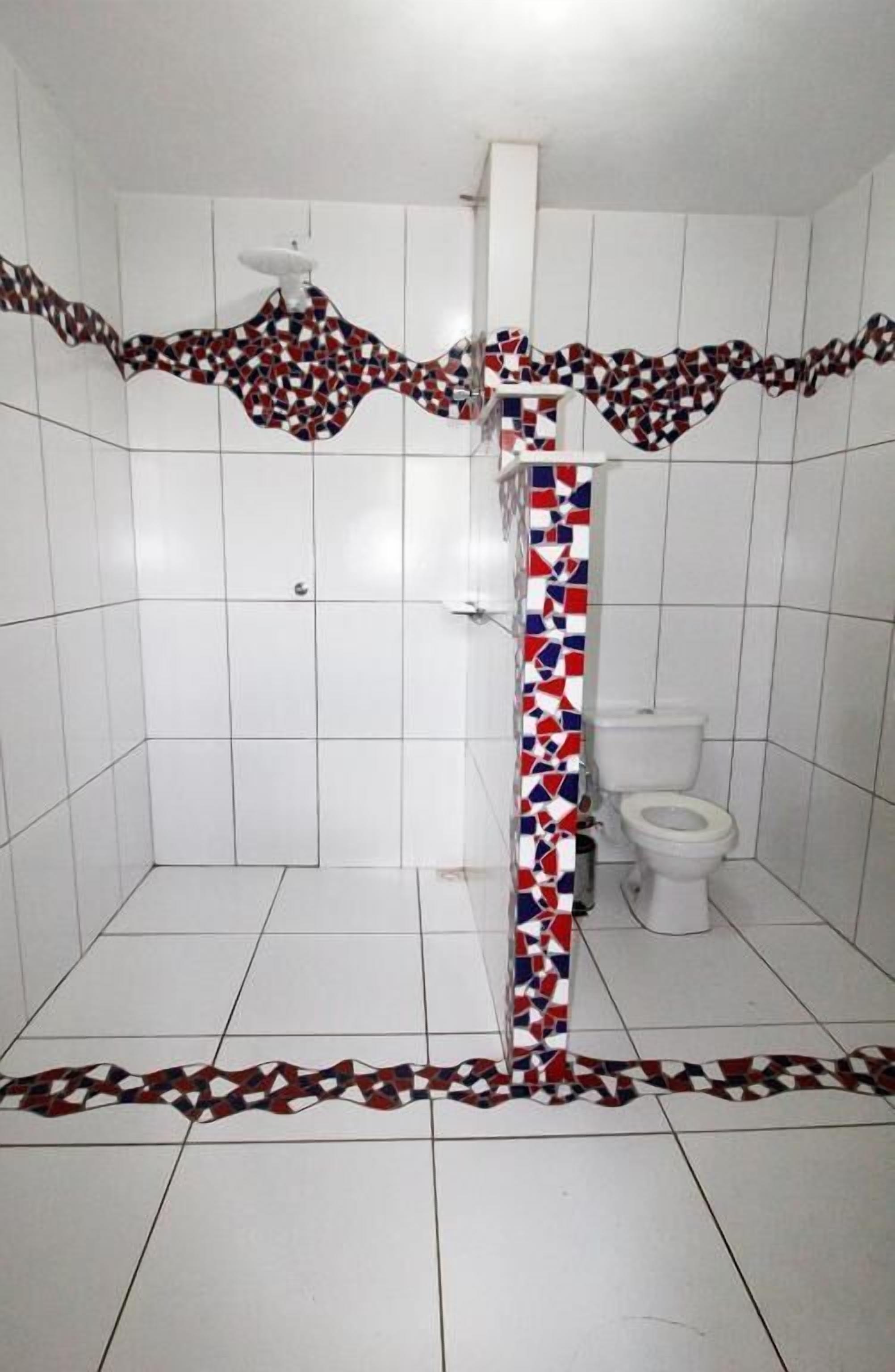 A bathroom with white tiled walls and floor, a shower with a white door, and a toilet.