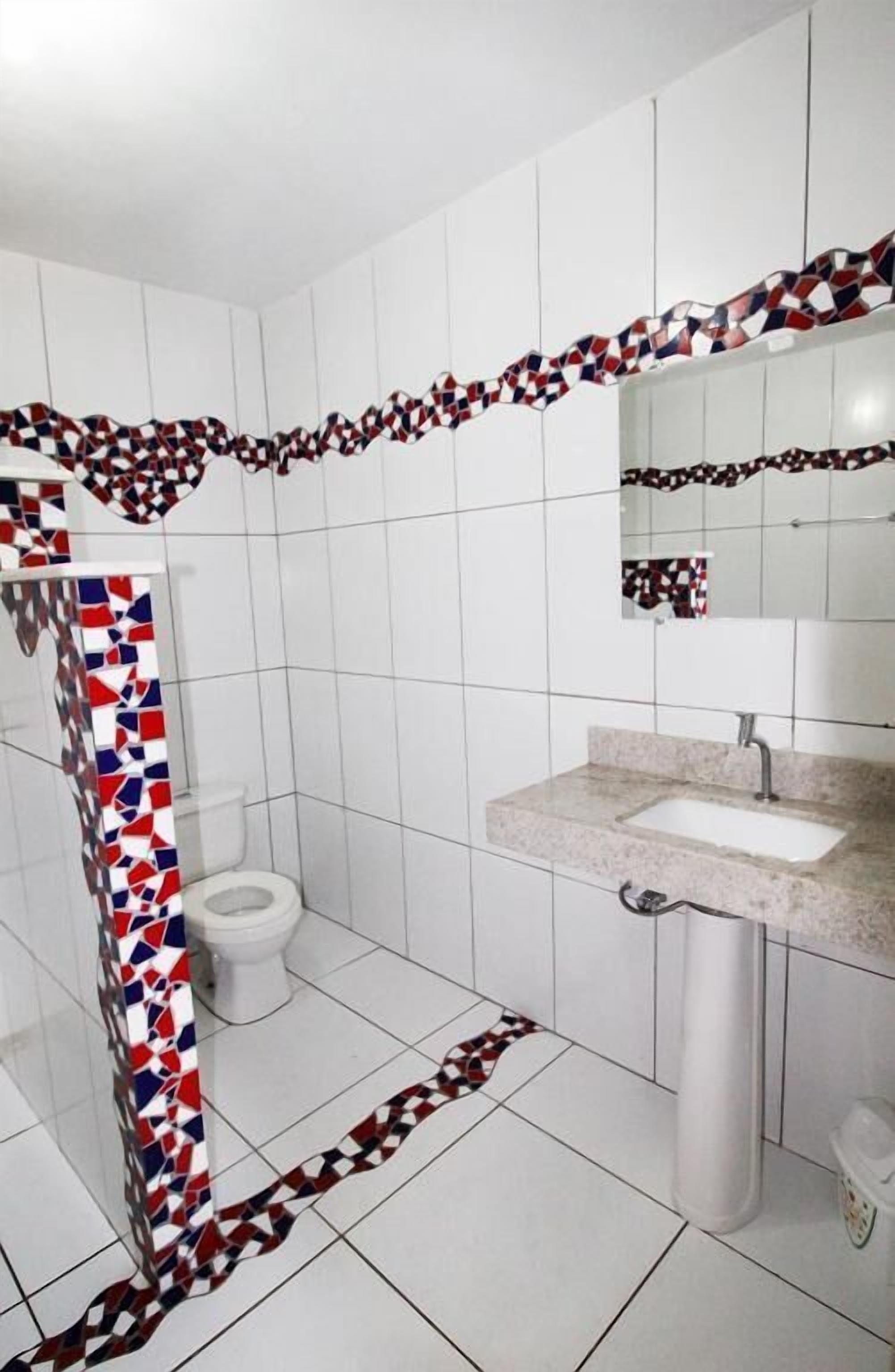 Een badkamer met witte betegelde wanden, een wit toilet, een wastafel met spiegel en een douchehoek.